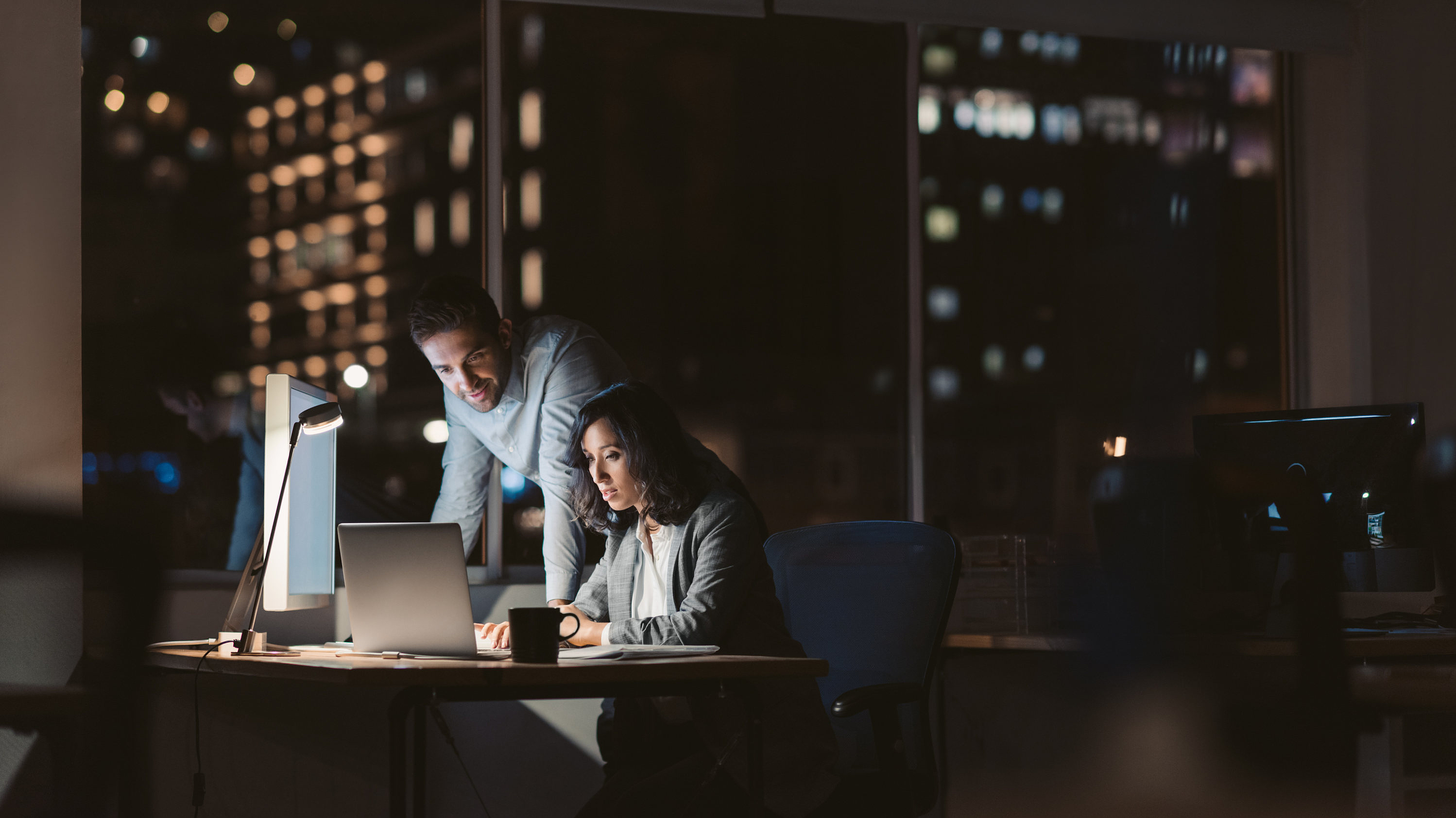Man and woman sitting in front of a glowing screen in a dark office