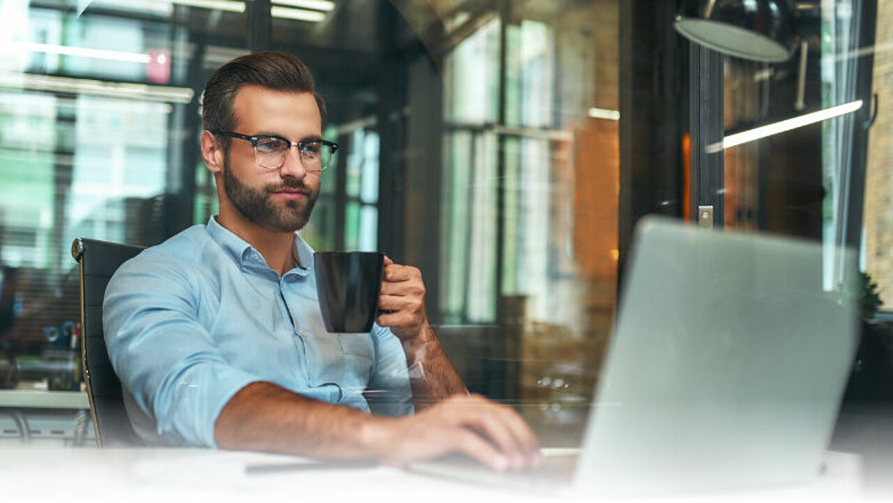 Mann mit Kaffeetasche vorm Laptop