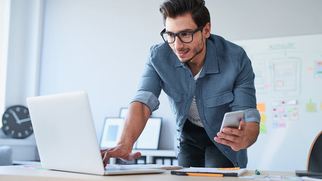 Man holding mobile phone and working on laptop