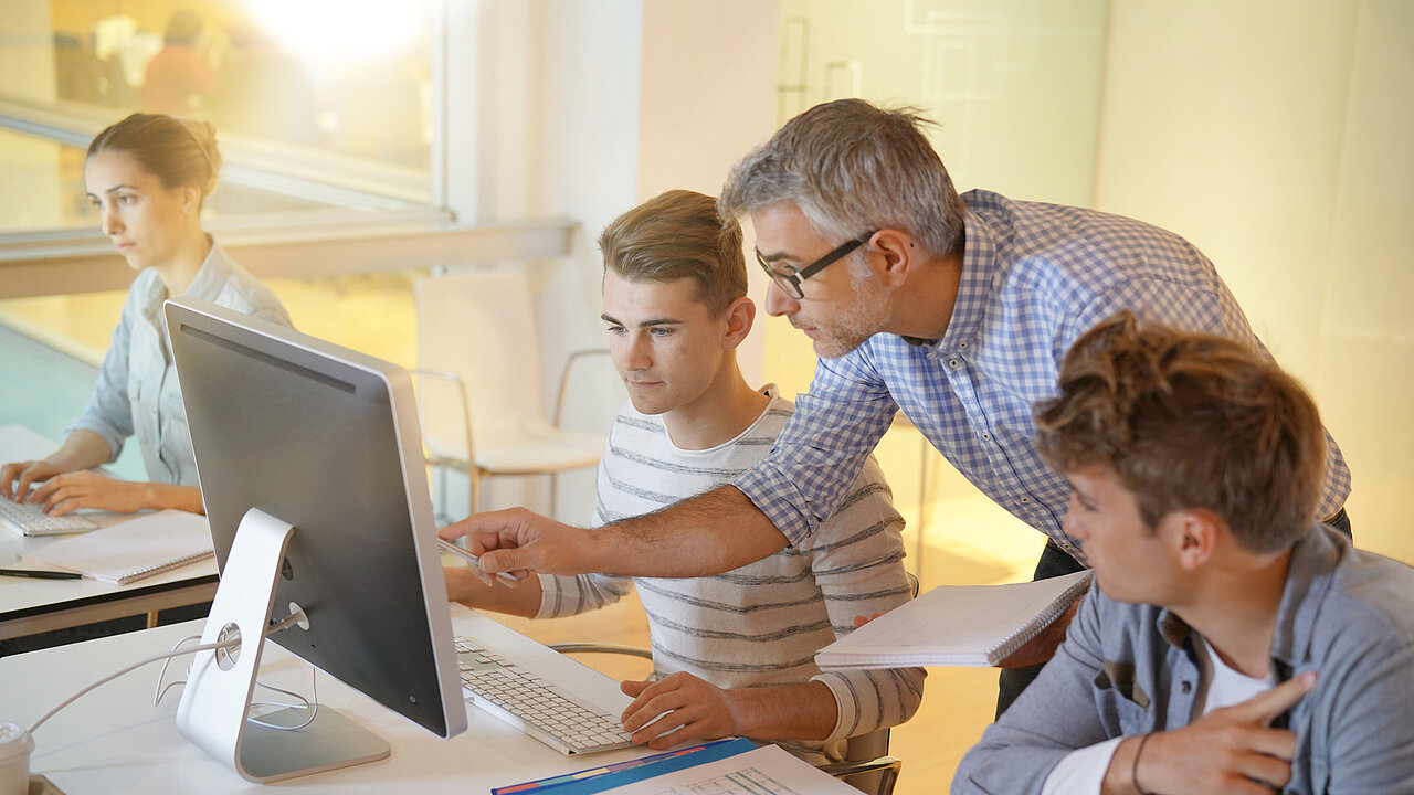 Die Schulen sicher digitalisieren mit Produkten von Securepoint. Lehrer erklärt Schülern den Umgang mit Computern.