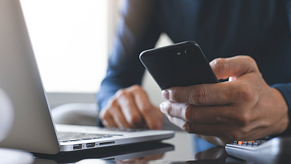 Securepoint Mobile Security mit MDM und Firewall to go. Mann hält ein Smartphone in der Hand und sitzt vorm Laptop.