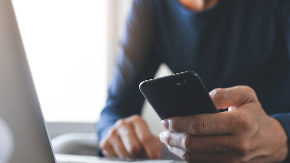 Man sitting at a laptop and holding a smartphone in his hand.