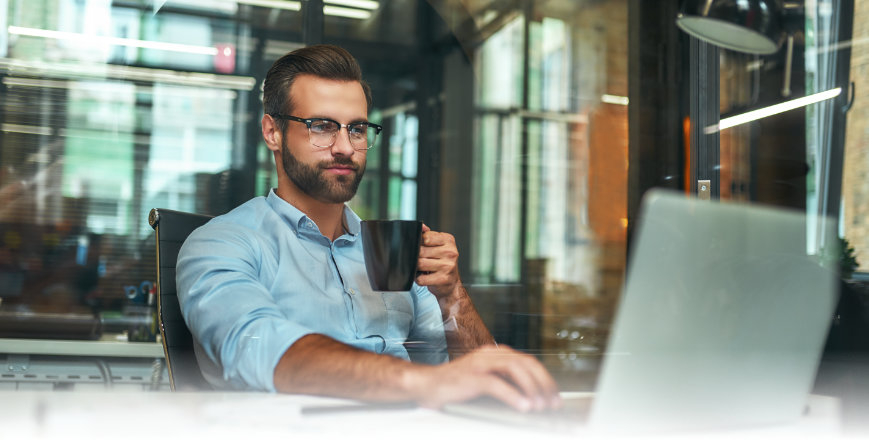 Mann mit Kaffeetasche vorm Laptop